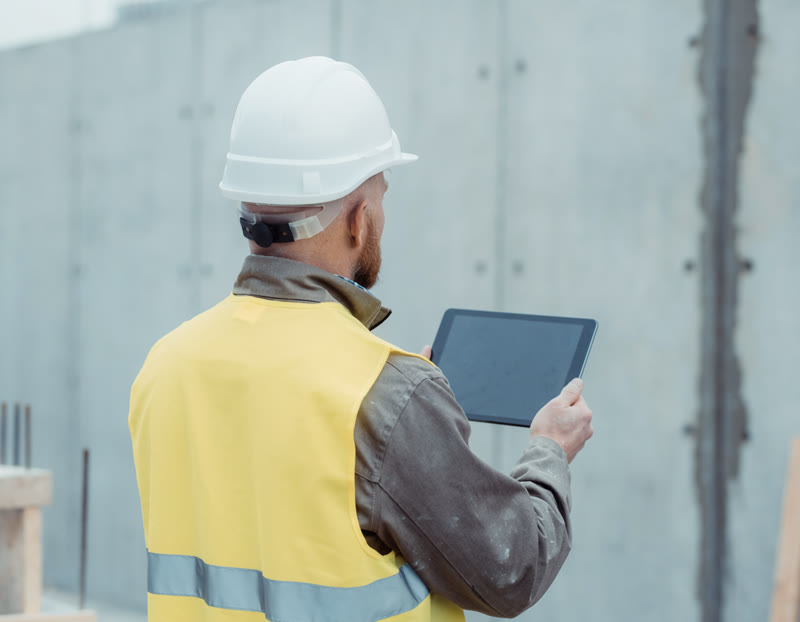 Håndværker med tablet foran en betonvæg på pladsen